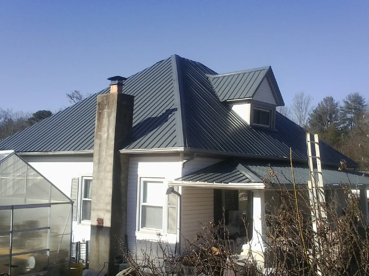 Dark blue standing seam metal roof on a white farmhouse with dormer — Slate & Tile Roof Repair by Roofing Brothers in Braithwaite