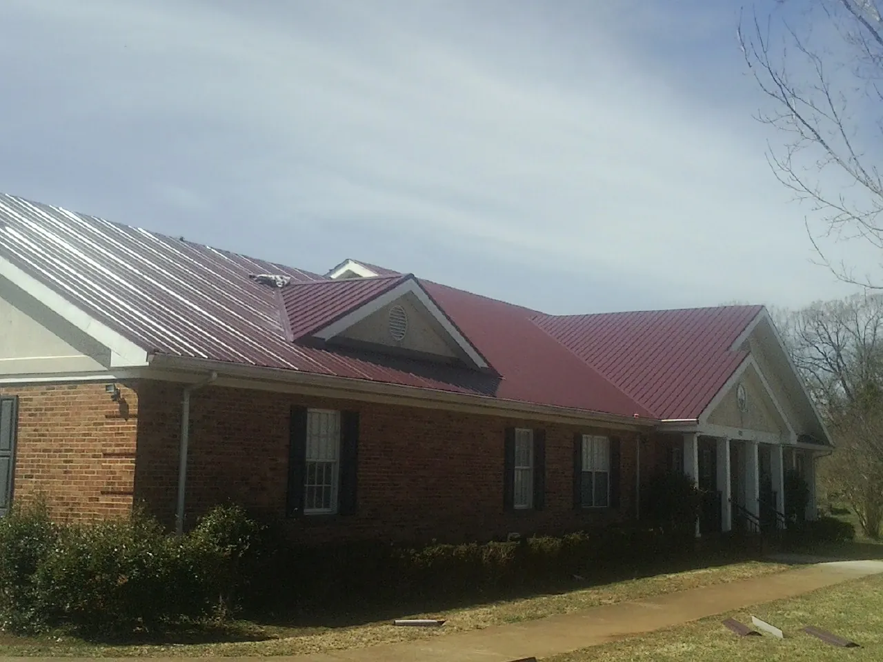 Red metal roof with gabled entries on a long brick building, from a Hail Damage Roof Repair job in Braithwaite