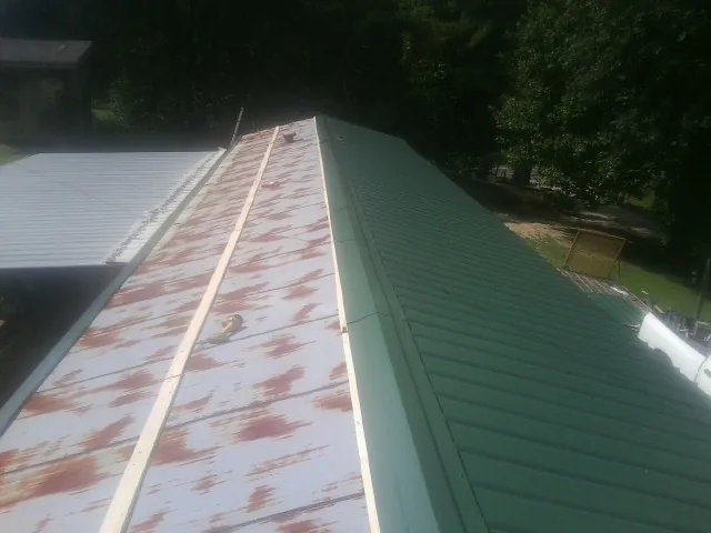 Old rusted panels beside newly installed green metal roofing — Wind Damage Roof Repair by Roofing Brothers in Braithwaite
