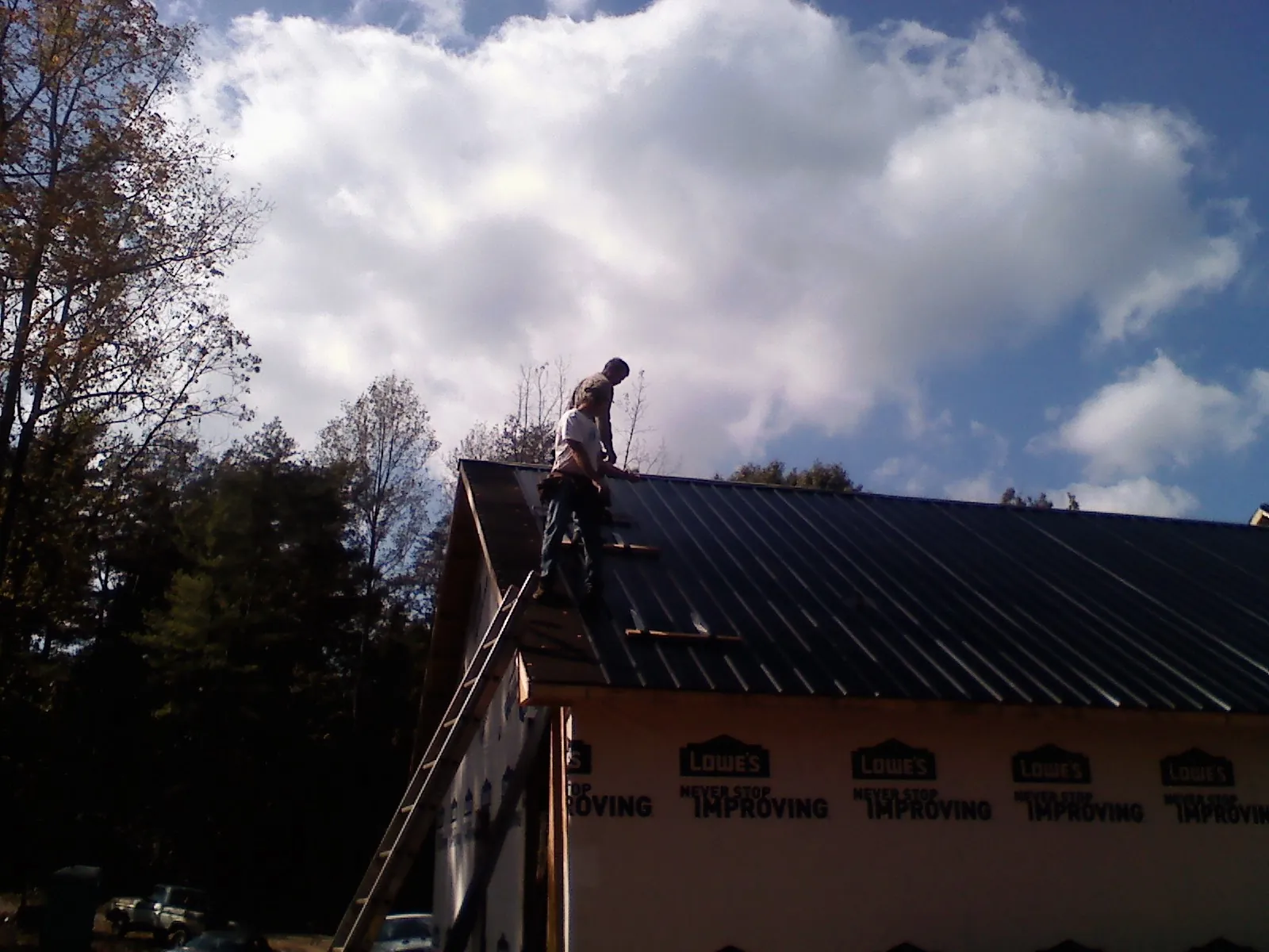 Roofer fastening dark metal panels high against a cloudy sky, from a Roof Inspection job in Braithwaite