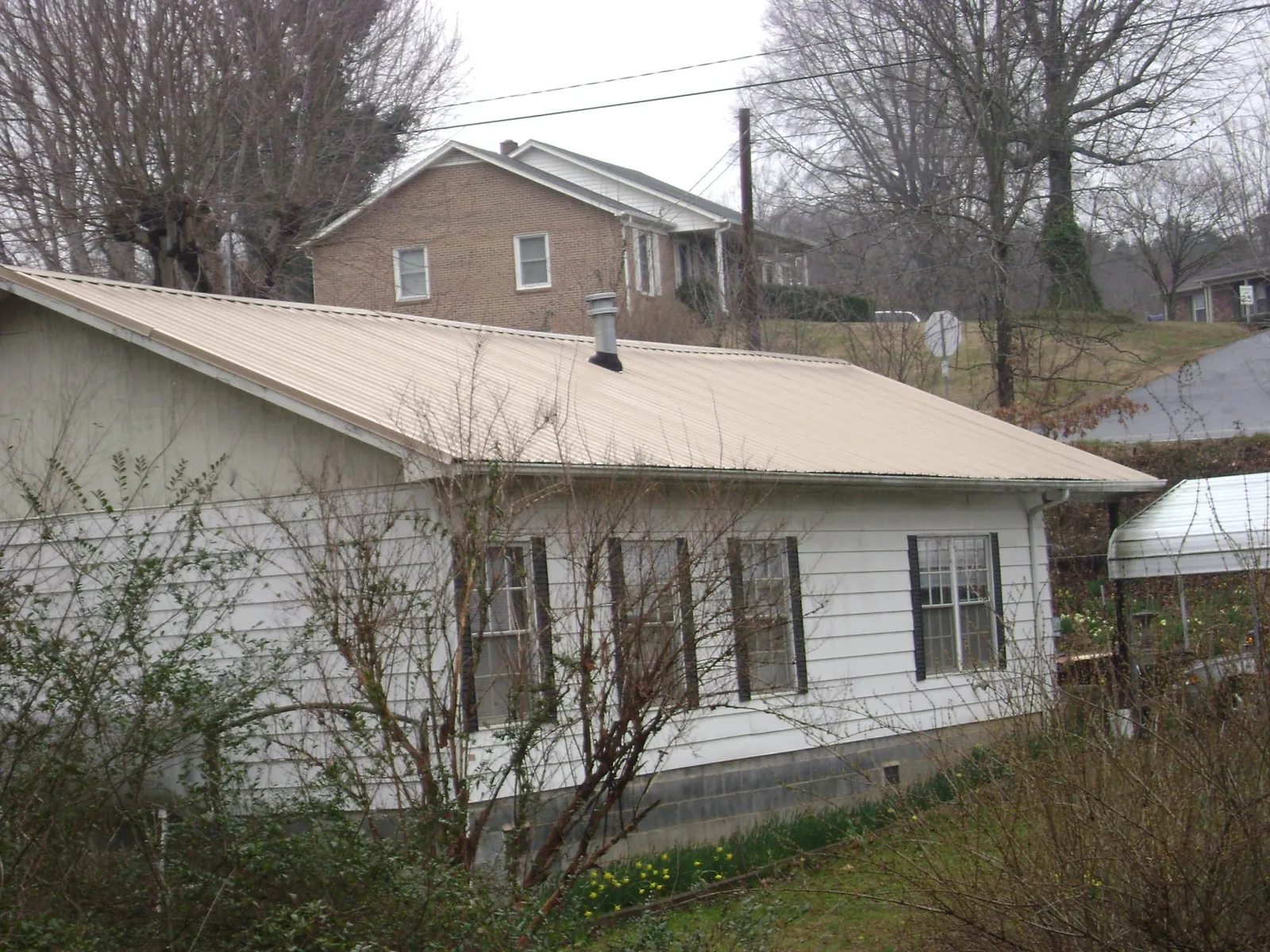 Tan metal roof on a white sided house set into a hillside — Commercial Roofing by Roofing Brothers in Braithwaite