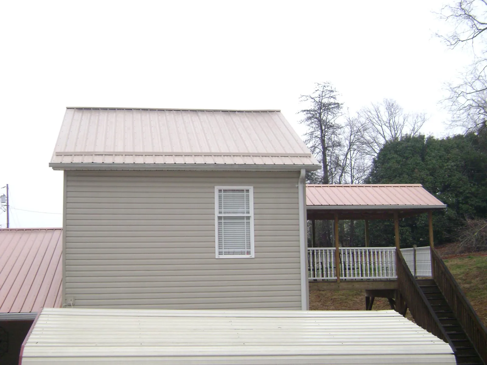 Tan metal roofs on a two story addition and attached porch, from a Roof Replacement job in Braithwaite